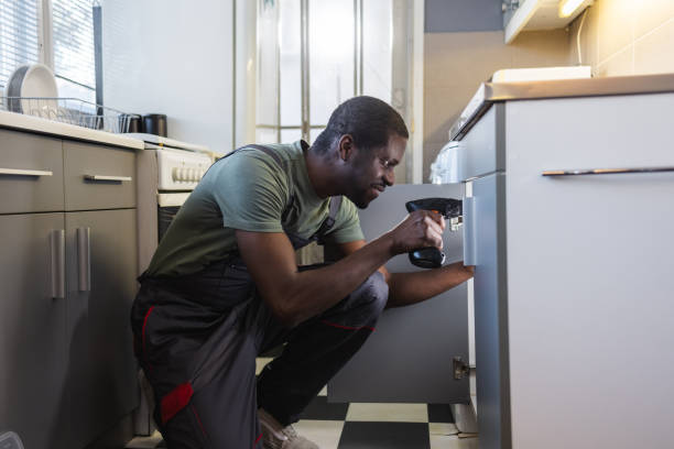 Photo of African American handyman in work clothes fixing leak in the kitchen sink